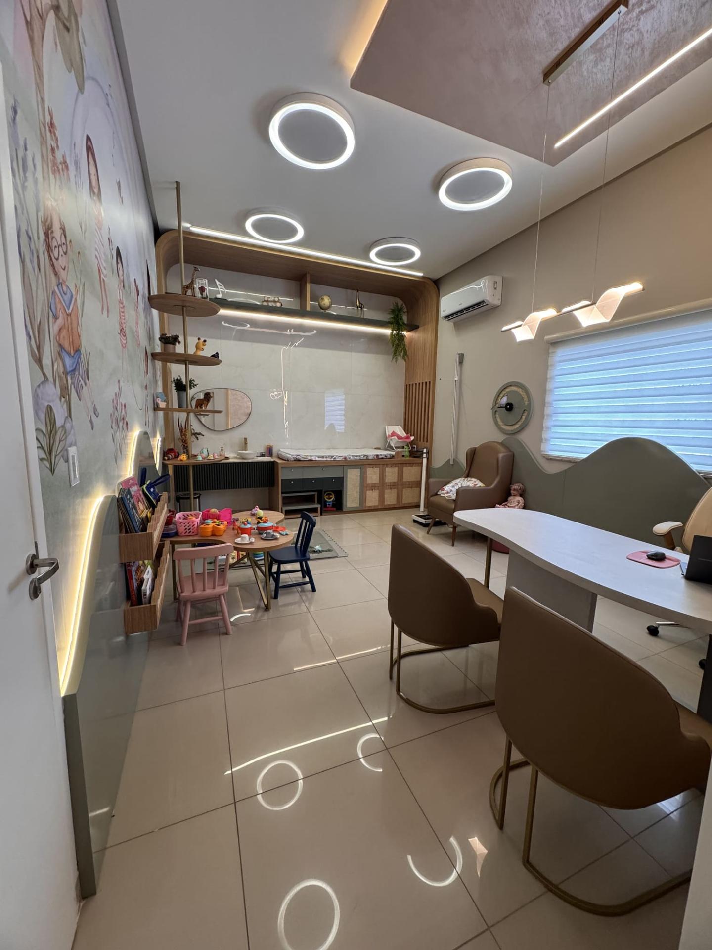 Vista geral do consultório com cantinho infantil e mesa de atendimento